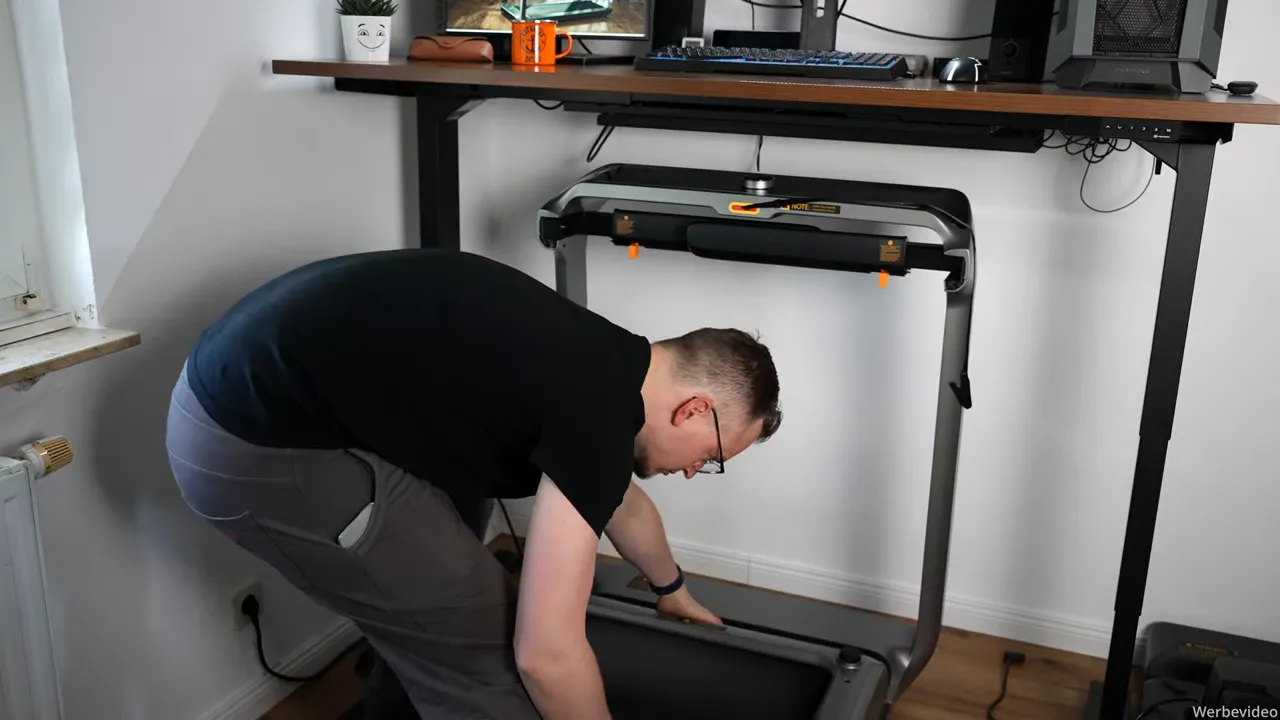 Person richtet das WalkingPad X218 unter einem höhenverstellbaren Schreibtisch ein, Laufband unter Tischplatte sichtbar