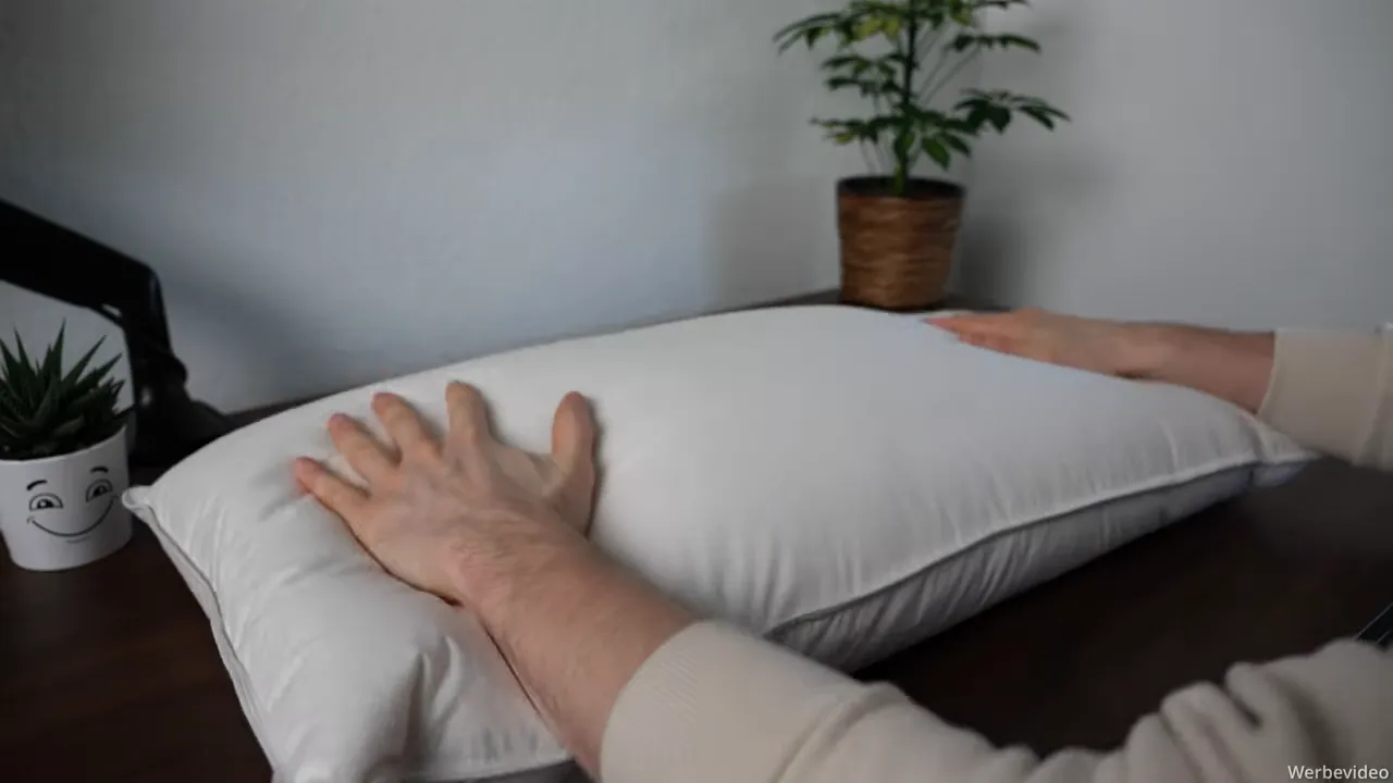 Hände drücken mittig auf das Daunenkissen zur Demonstration der Nachgiebigkeit
