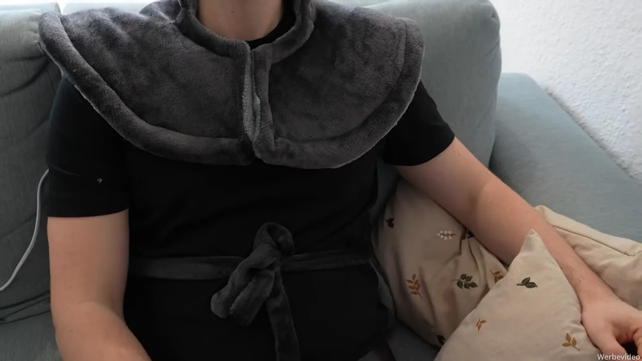 Heizdecke für Rücken, Schulter & Nacken von Bob & Brad im Test 11 Person trägt Bob & Brad Heizdecke als Schulter-/Nackenwärmer auf dem Sofa, Bauchgurt sichtbar