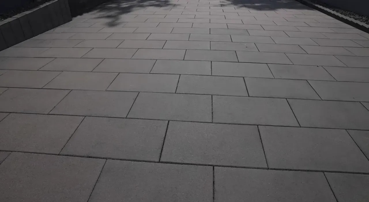 Langer sauberer Seitenweg mit gleichmäßigen grauen Steinplatten entlang einer Hauswand