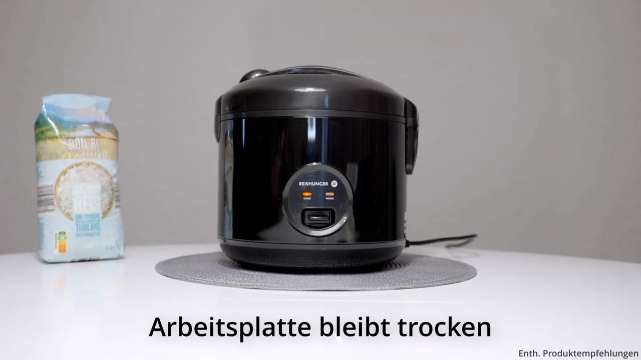 Schwarzer Reiskocher auf sauberer weißer Arbeitsfläche mit eingeblendeter Aufschrift Arbeitsplatte bleibt trocken