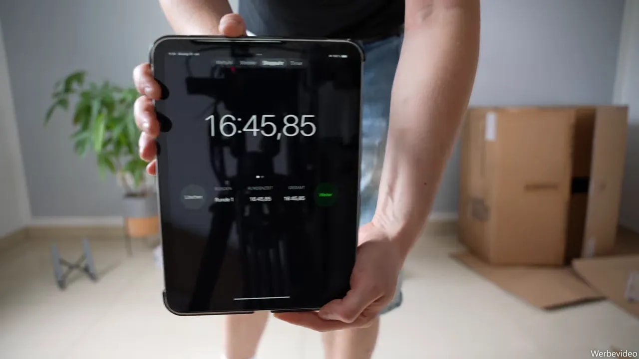 Tablet mit gemessener Aufbauzeit von 16 Minuten und 45 Sekunden vor dem aufgebauten Bürostuhl