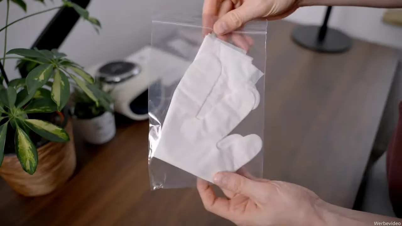 Hand hält eine Packung mit weißen Einweghandschuhen vor dem Handmassagegerät
