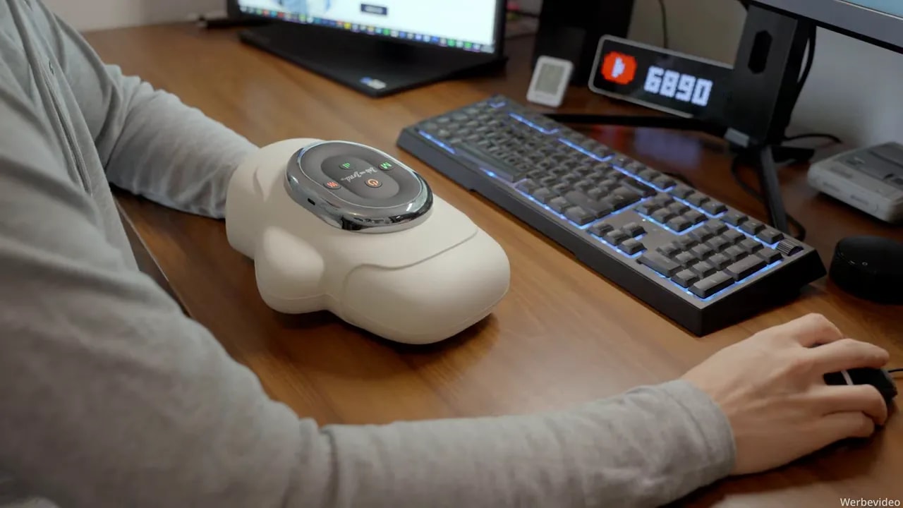 Person nutzt das Handmassagegerät am Schreibtisch neben Tastatur und Computermaus