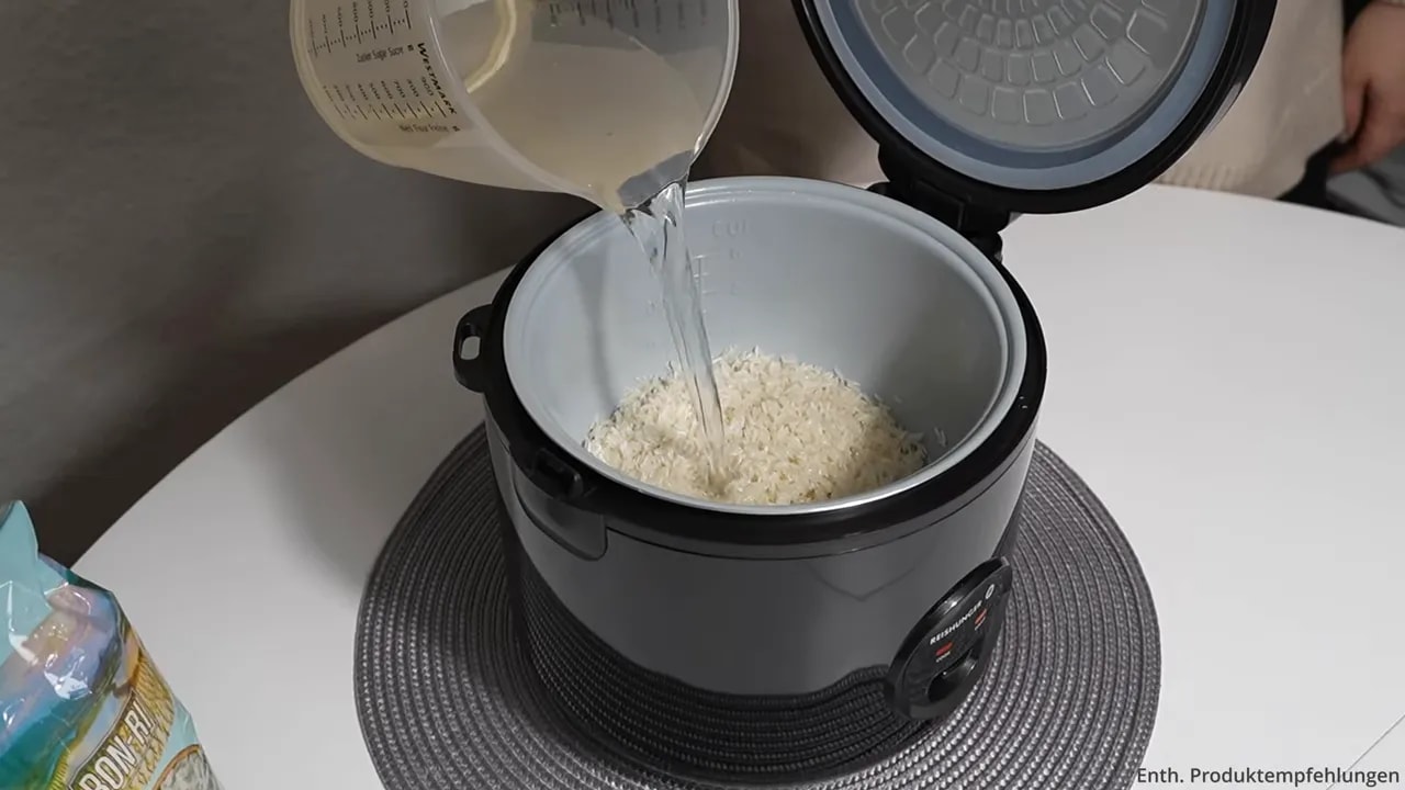 Wasser wird aus einem Messbecher in den Innentopf mit Reis gegossen