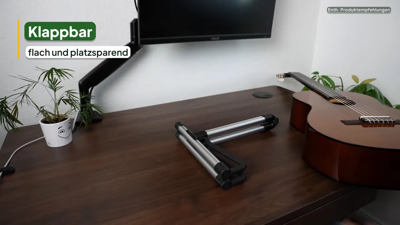 Flach zusammengeklappter Aluminiumständer auf einem Tisch neben einer liegenden Konzertgitarre